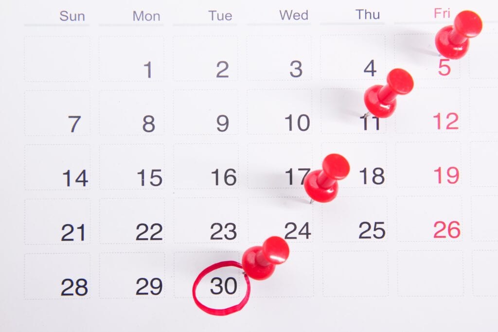 Ein Kalender in welchem an einem Tag der Woche rote Stecknadeln stecken